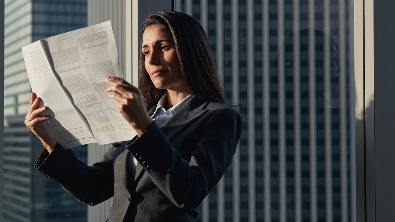 A chief financial officer reviewing a one-page decision document by an office window